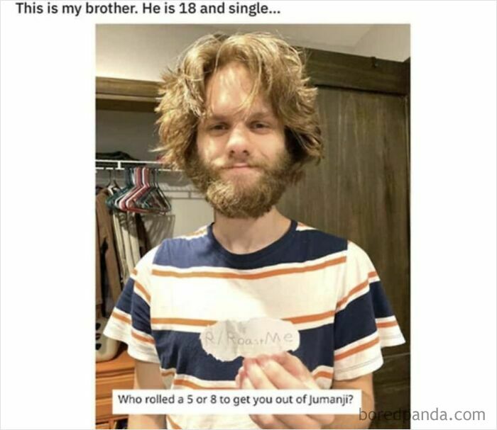 A man with a beard and shaggy hair holds a sign, with a clever clapback about being from Jumanji.