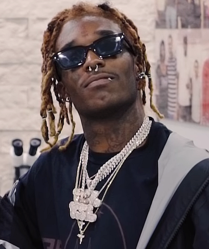 A close-up of Lil Uzi Vert, a rapper with dreadlocks and sunglasses, wearing multiple diamond chains as a highlight of his career.