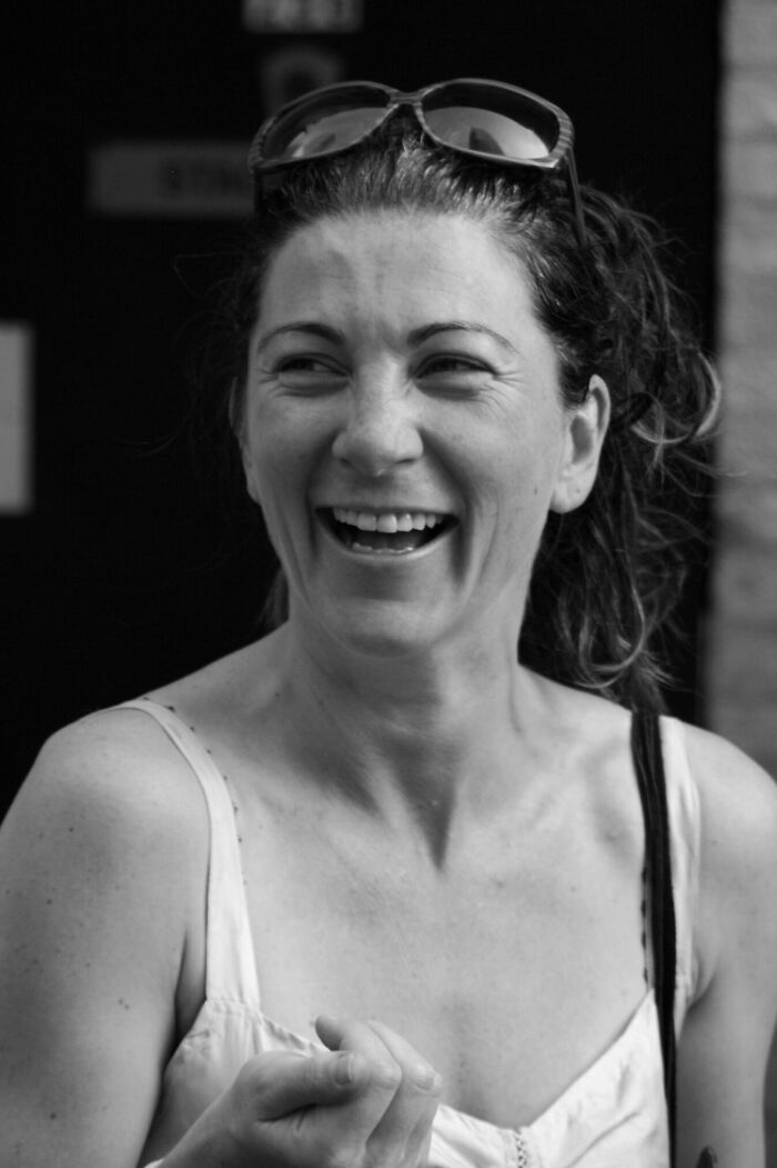 A black and white image capturing Eve Best, smiling joyfully, with sunglasses atop her head, highlighting her career.