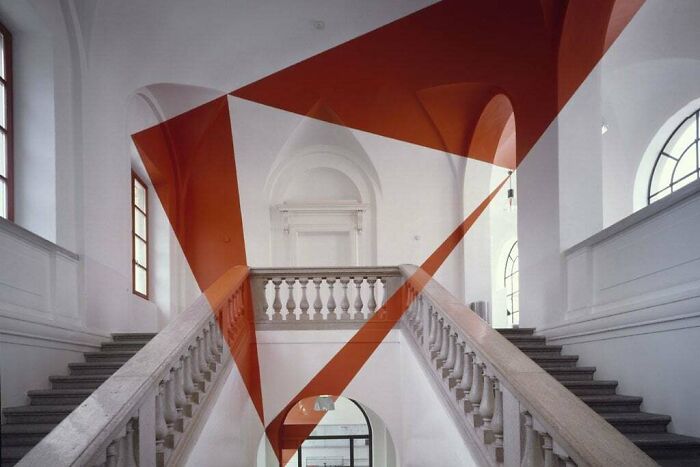 An optical illusion of red geometric shapes overlaid on a grand white staircase, a real photo that makes your brain question if it was edited.