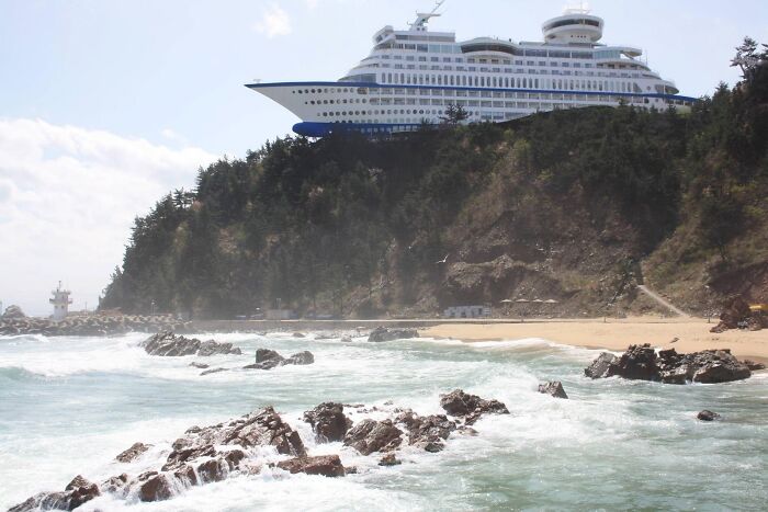 A large cruise ship hotel on a cliff overlooking a beach, a real photo that makes your brain question if it was edited.