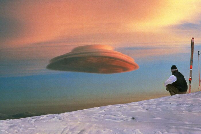 A skier looks at a lenticular cloud resembling a UFO in the sky, making your brain question if it was edited.
