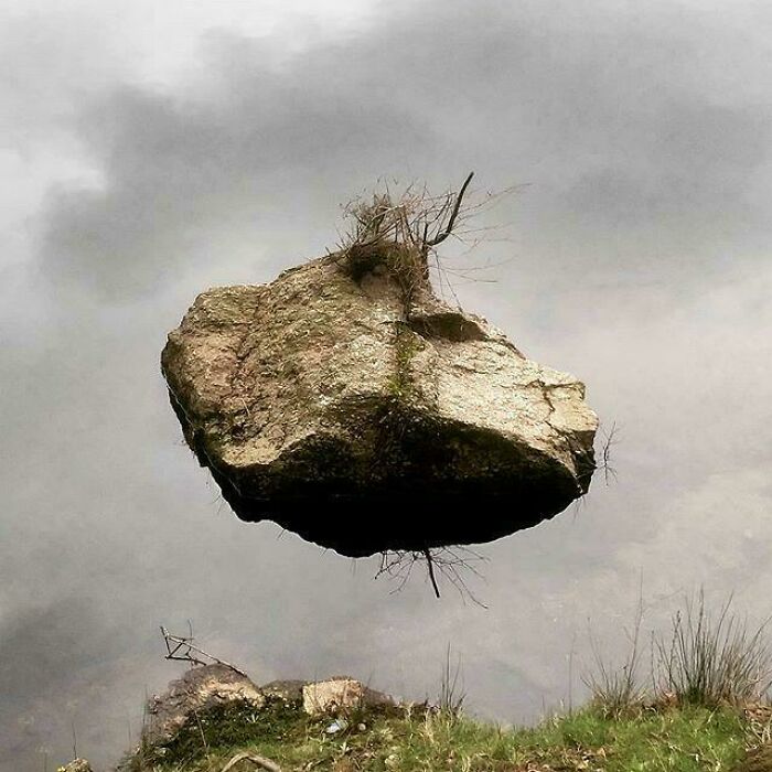 A large rock seemingly floating in the air above water, a real photo that makes your brain question if it was edited.