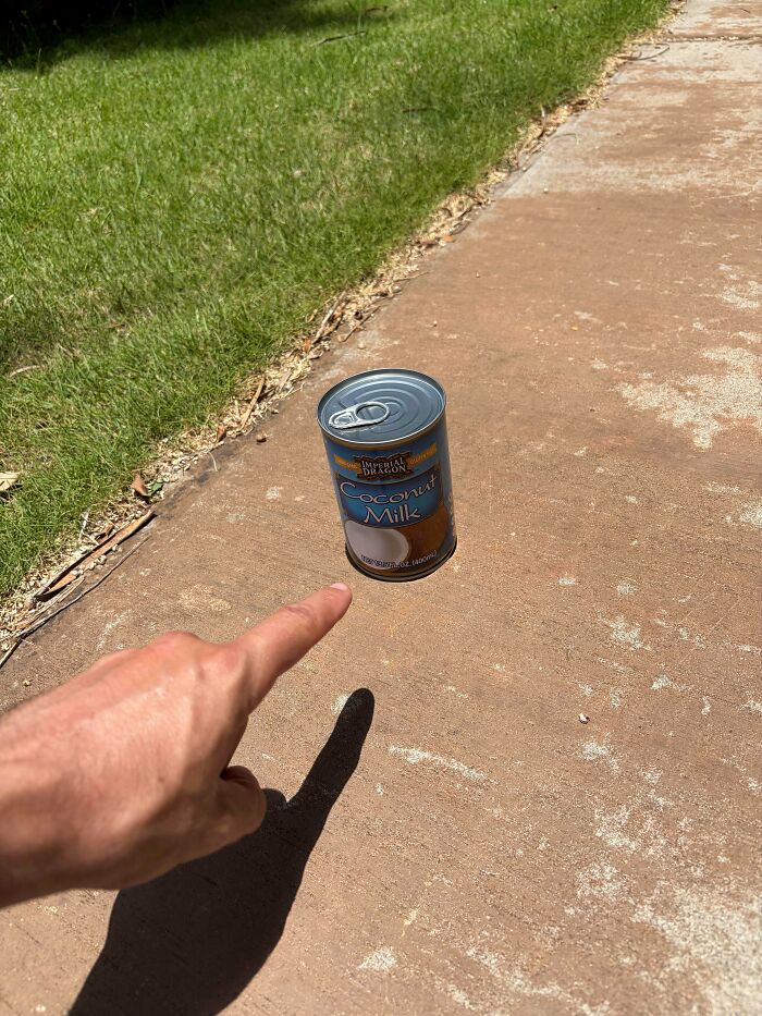 Real photos of a hand pointing at a can of coconut milk on concrete, creating a visual illusion, making you question if edited.