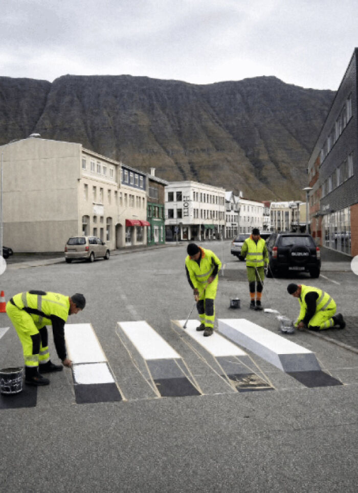 Workers painting a 3D crosswalk on a street, a real photo that makes your brain question if it was edited.