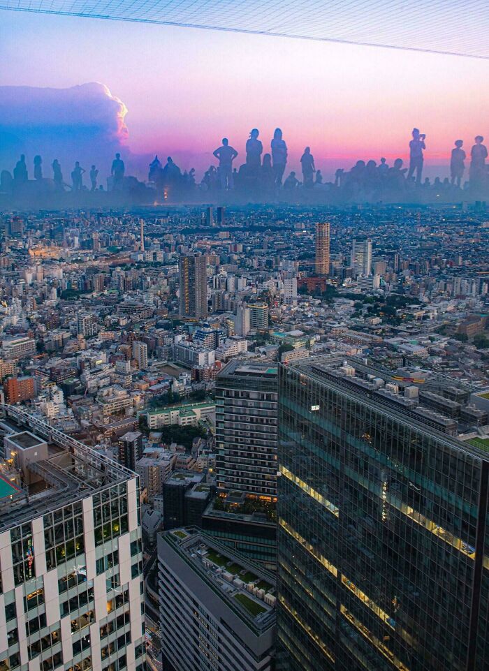 An expansive city skyline with silhouettes of giant people in the distance against a colorful sunset, a real photo that questions editing.