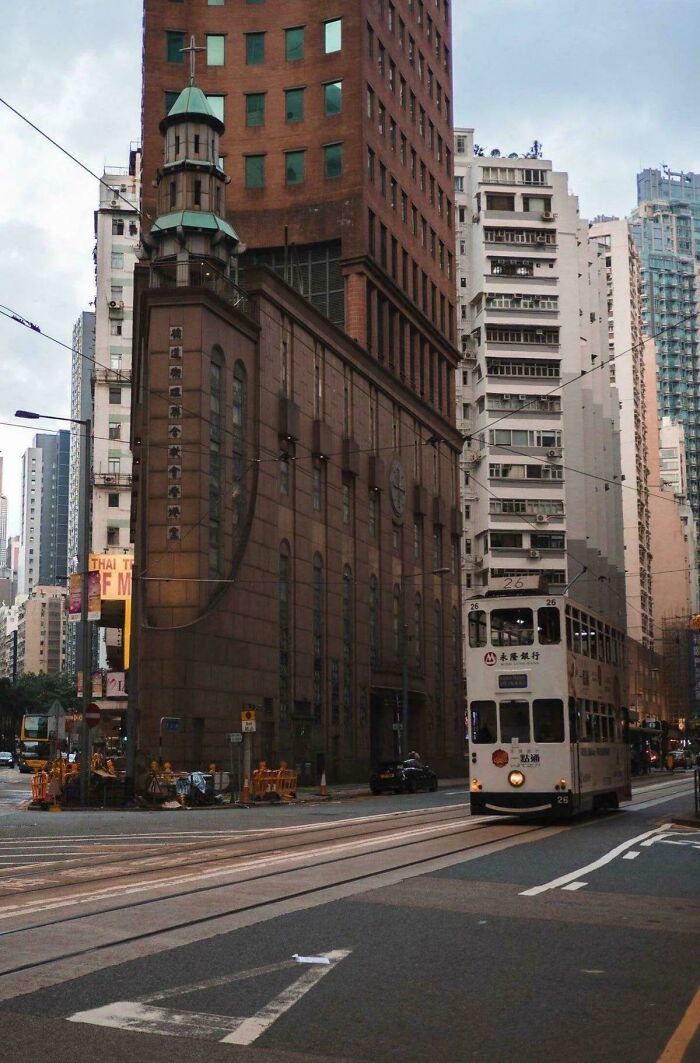 A narrow, historic-looking building with a spire nestled between modern skyscrapers, with a tram in the foreground, a real photo that questions editing.