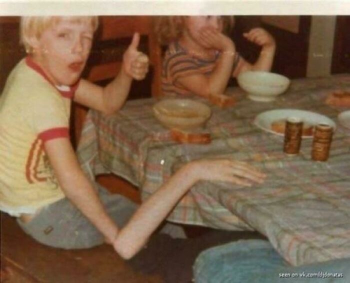 A young child at a table with an unnaturally long arm giving a thumbs-up, creating a bizarre visual. Real photos that make your brain question if they were edited.