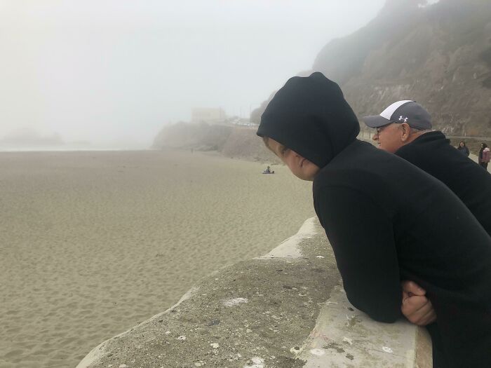 Real photos of people looking out at a foggy beach, making the brain question if they were edited.