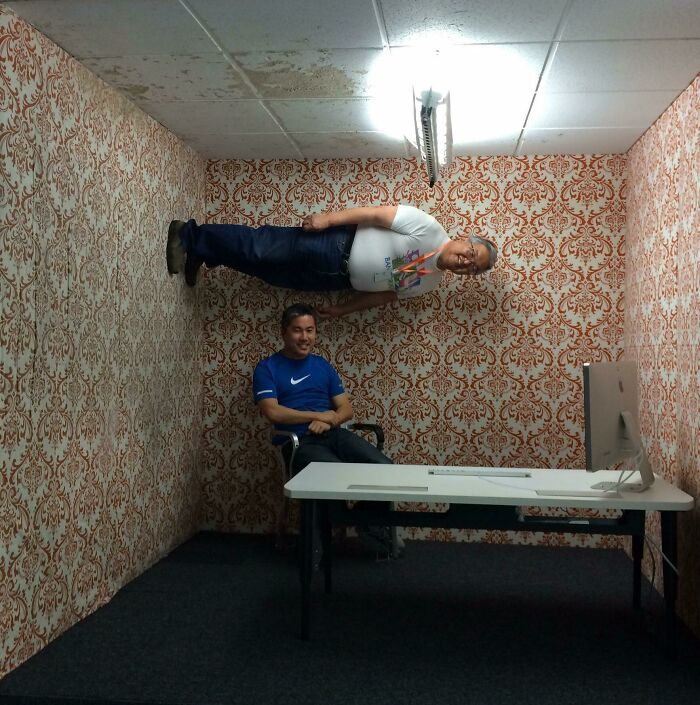 Real photos of a man lying sideways on a wall with another man sitting on a chair, making the brain question if they were edited.