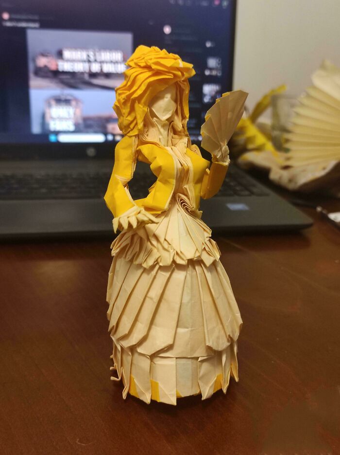 An intricately folded origami figure in a yellow dress, a real photo that makes your brain question if it was edited.