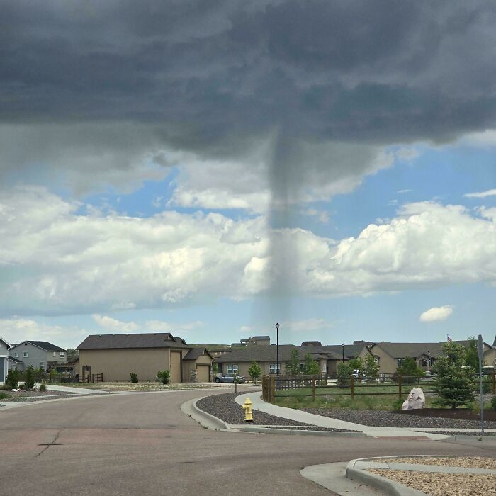 A dramatic shaft of rain falling from a cloud over a neighborhood, a real photo questioning reality.