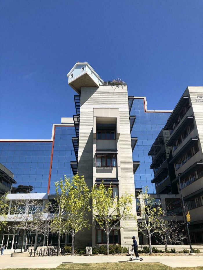 A small house precariously perched on top of a tall building, making the brain question if the photo was edited.