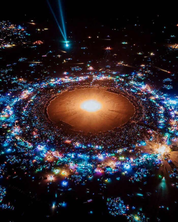 An aerial view of a vibrant, illuminated night festival with a bright center, making the brain question if the photo was edited.