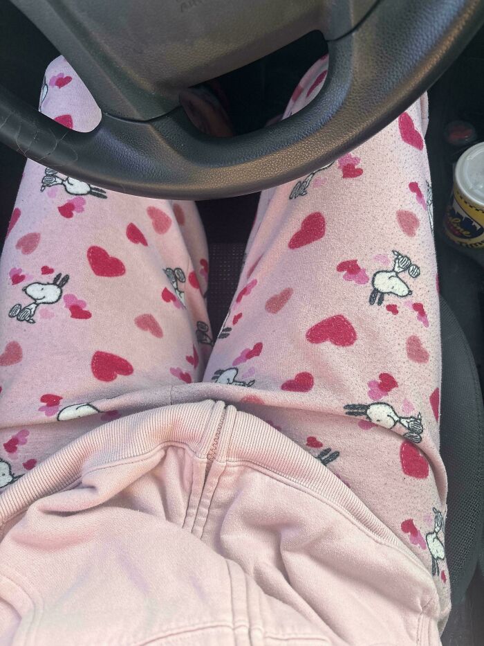 A person in pink pajamas with sheep and hearts driving, forgetting to change, ruining their day.