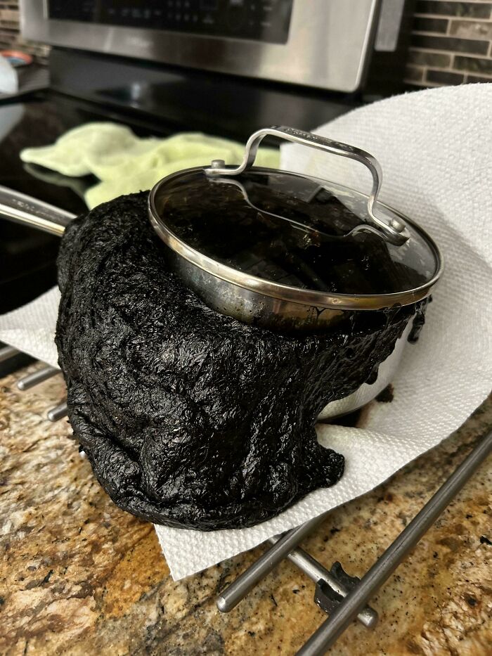 A severely burnt pot of food, overflowing with black residue on a counter, ruining an entire day.