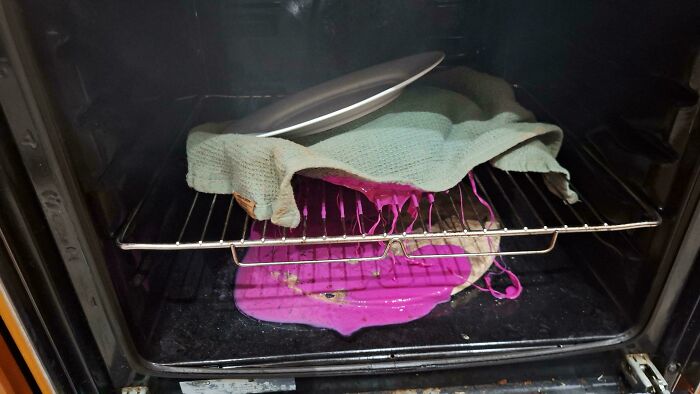 Melted pink goo and a cloth in an oven, showing something important was forgotten.