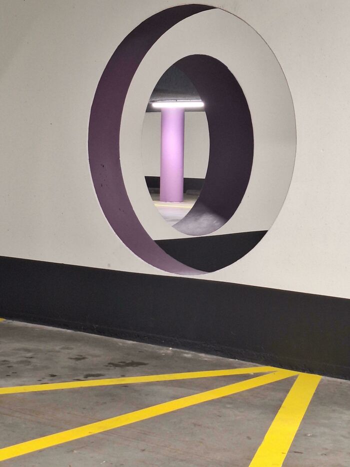 Real photo of a purple pillar seen through a circular cutout in a wall, an optical illusion making your brain question perspective.