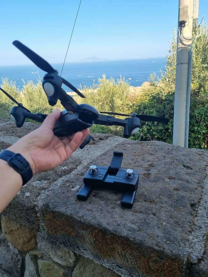 A person holding a drone outdoors with a controller nearby, potentially ruining the entire day by forgetting a crucial part.