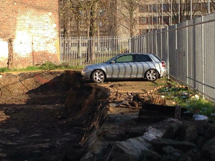 A silver car parked precariously close to a large ditch, almost ruining the entire day.
