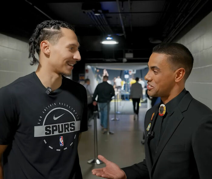 Two men, one in a Spurs t-shirt and the other in a suit, smile and converse, potentially discussing an exposed cheater.