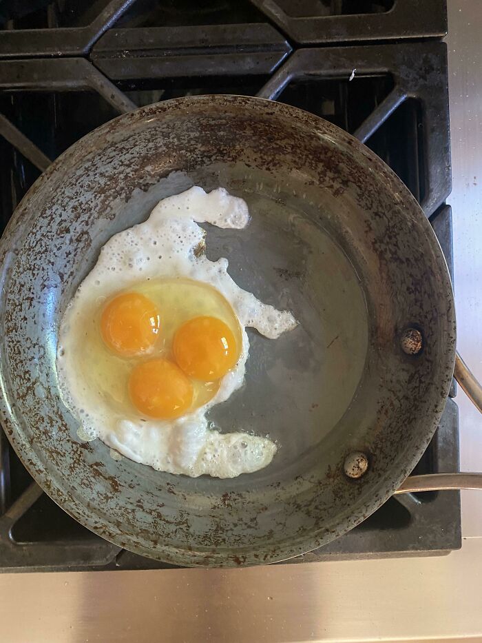 A rare occurrence of three egg yolks in one cracked egg in a frying pan.
