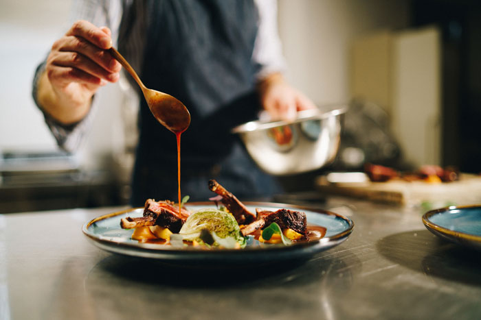 A chef expertly drizzles sauce over a plated dish, an example of surprisingly affordable culinary experiences.
