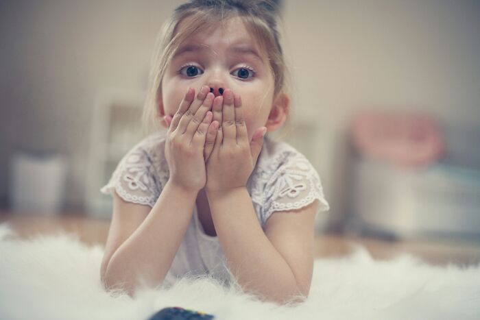A young child with a surprised expression, hands covering mouth, as if asking kids questions.