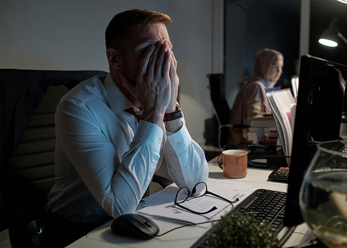 A man holding his face at a desk, stressed about dementia symptoms, working late. A man holding his face at a desk, stressed about dementia symptoms, working late.