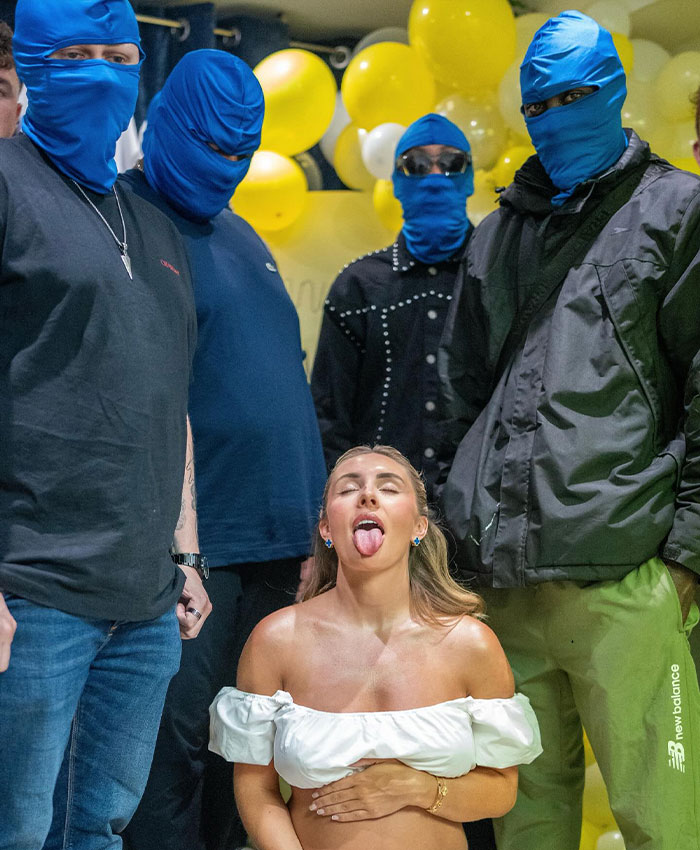 Bonnie Blue on her knees, sticking out her tongue, surrounded by men in blue masks during a baby-themed stunt.