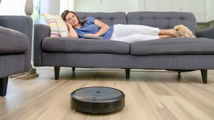 A woman napping on a couch while a robot vacuum cleans, highlighting comfort and convenience. Discussing family pictures.