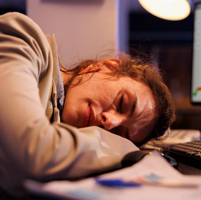 A tired woman sleeping with her head on her arm at a desk, sharing truths women learned.