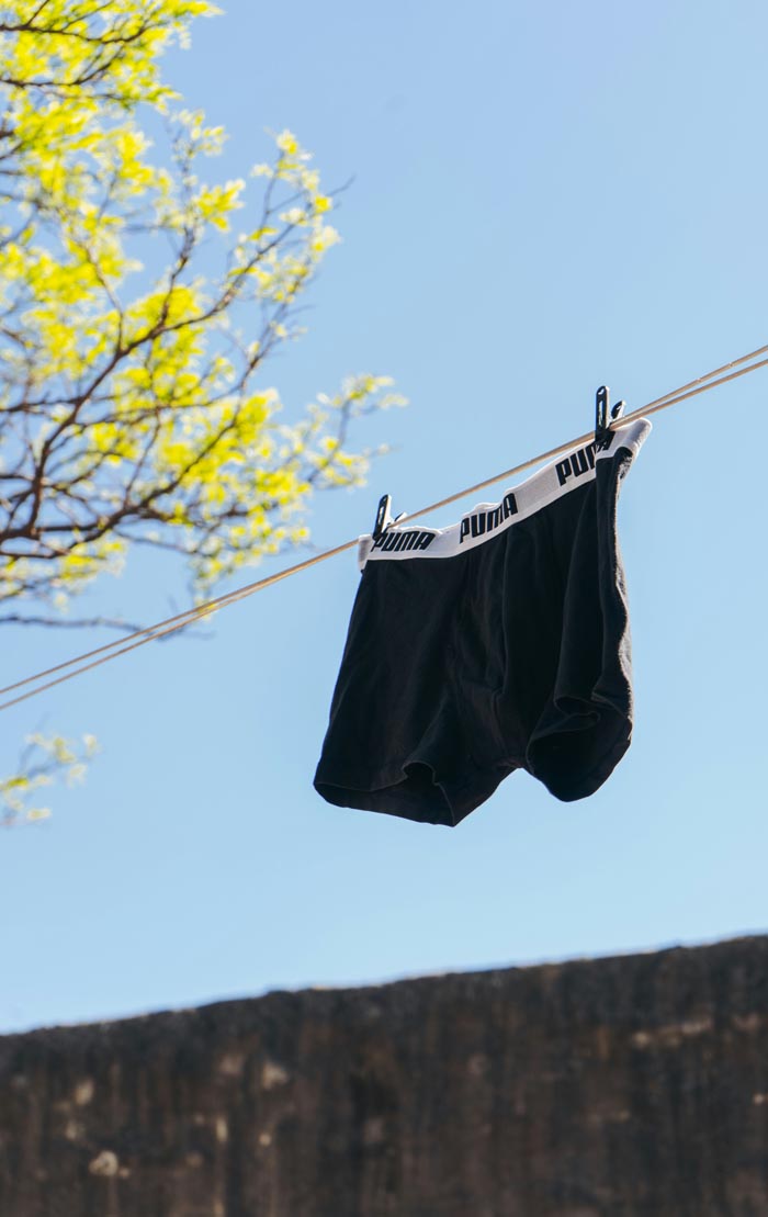 A pair of black men's underwear hanging on a clothesline against a clear blue sky, highlighting unhygienic practices.