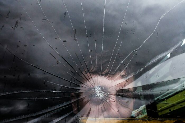 A close-up of a shattered car windshield with a person's reflection, a serendipitous moment captured by a street photographer.