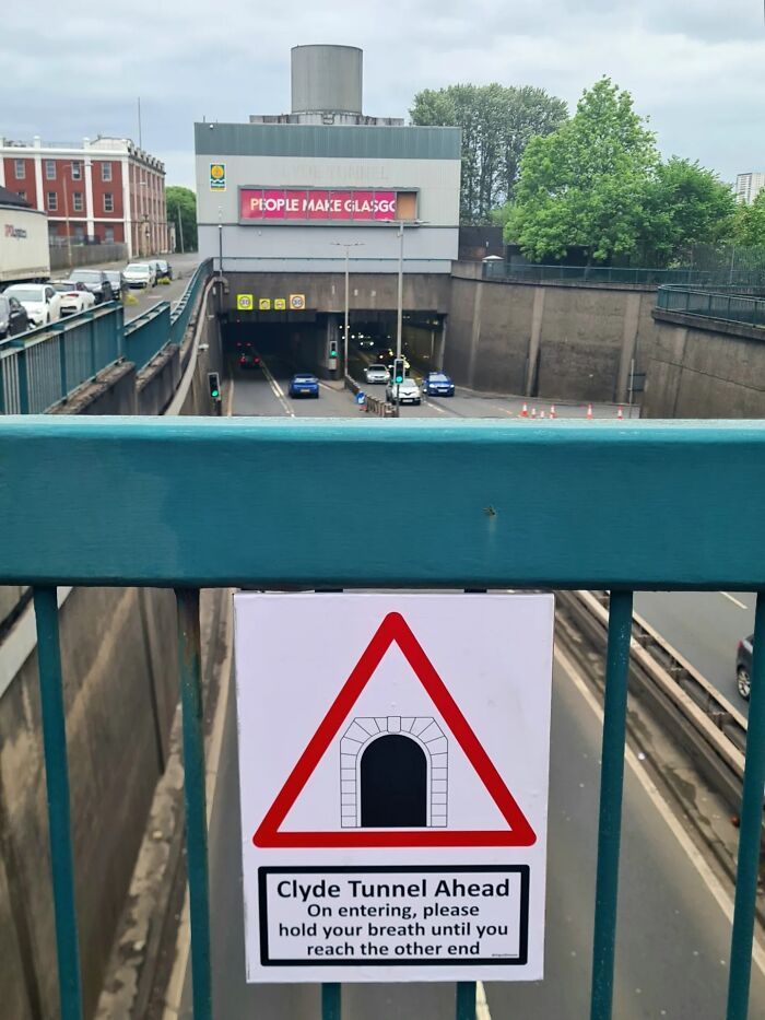 Absurd sign for Clyde Tunnel, asking to hold breath, overlooking a busy tunnel entrance.