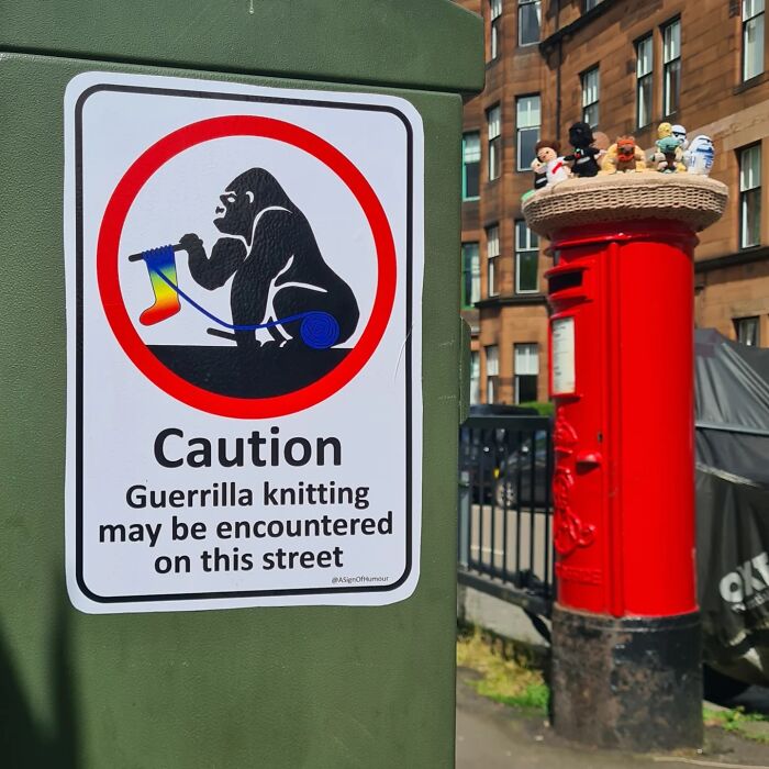 Absurd sign with a gorilla knitting, warning about guerrilla knitting on the street, near a red post box.