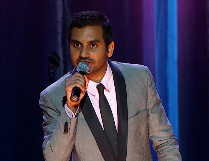 Aziz Ansari on stage with a microphone, facing criticism about his marriage and lifestyle revelation. Aziz Ansari on stage with a microphone, facing criticism about his marriage and lifestyle revelation.