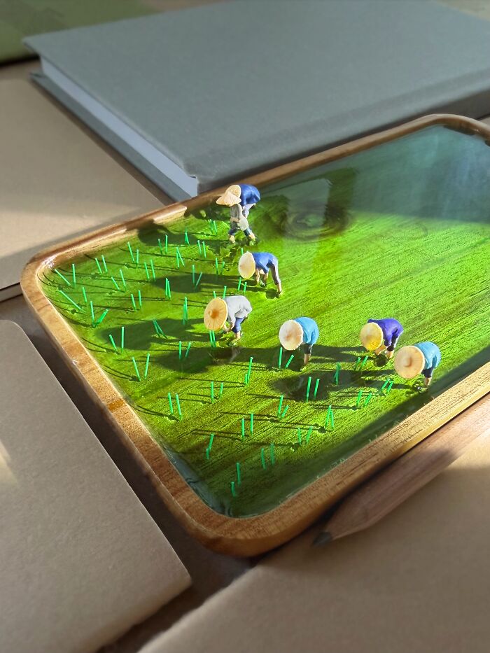 Artist Derrick Lin turns his office desk into intricate diorama sets, showing tiny figures working in a rice paddy.