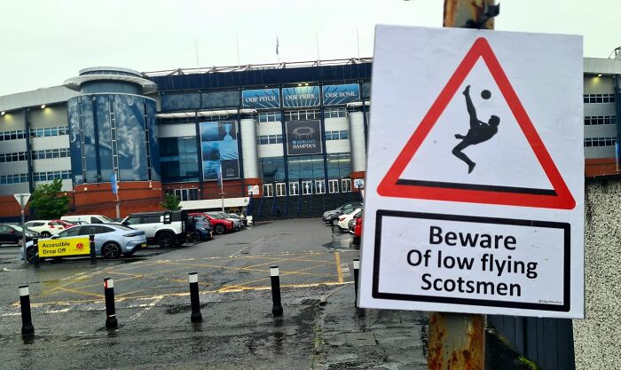Absurd signs: A warning sign about low flying Scotsmen with a soccer player silhouette near a stadium.