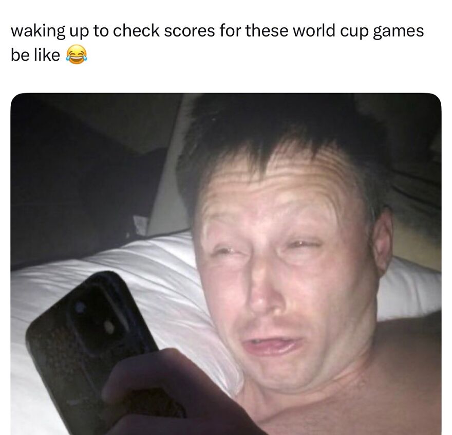 A man with a dazed expression in bed, checking his phone for World Cup scores, showing hilarious World Cup memes chaos.