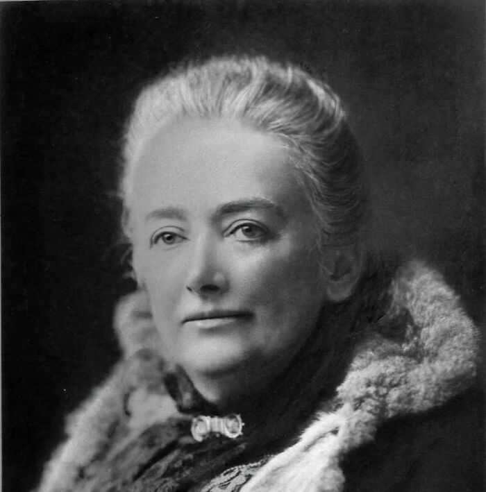 A black and white portrait of a woman with grey hair, wearing a fur-collared coat, representing overlooked women in history.