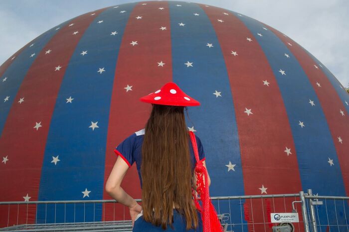 A woman wearing a red mushroom hat looks at a red and blue striped dome with stars, a serendipitous moment captured by a street photographer.