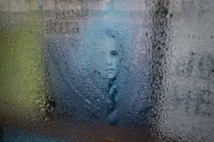 A street photographer captures a serendipitous moment of a person looking through a steamy window in everyday life.
