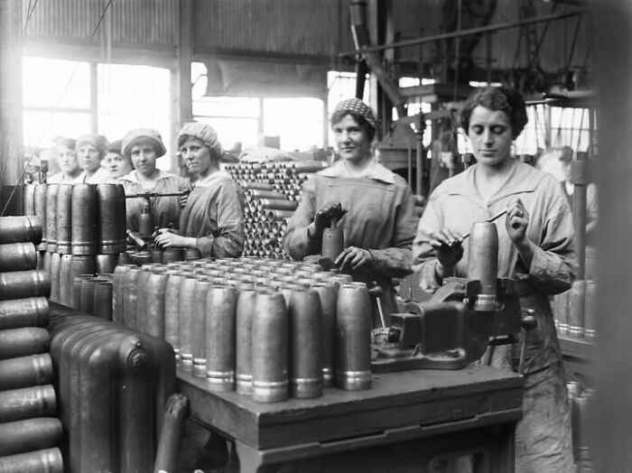 Several women working in a factory, surrounded by large shell casings, highlighting overlooked women in history.