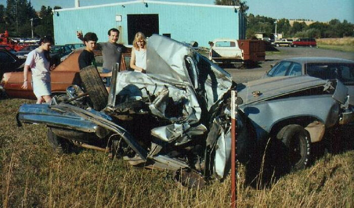 Four people standing around a severely mangled car after a rare and devastating accident.