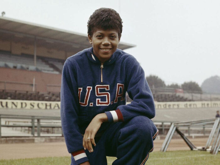Wilma Rudolph, one of the overlooked women in history, kneels on a track in a USA tracksuit.