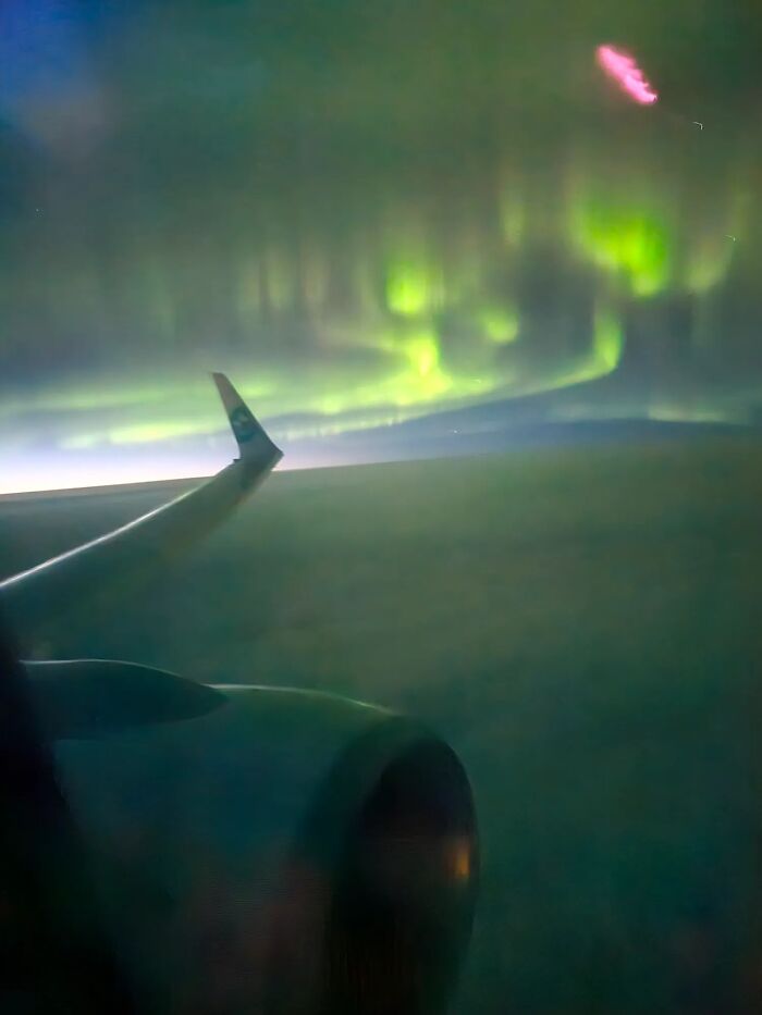 Airplane wing soaring above green aurora borealis, a rare natural phenomenon that has happened to them.