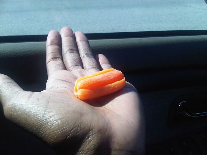 A hand holding two baby carrots fused together, showcasing one of the rarest things that have ever happened to them.