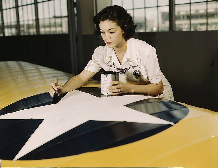 A woman painting a white star on a yellow airplane wing, highlighting overlooked women in history.