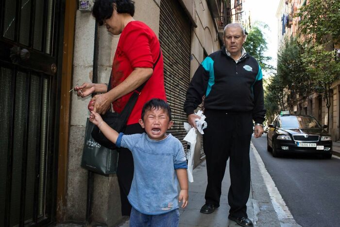 A street photographer captures a serendipitous moment of a crying child with adults on a street in everyday life.